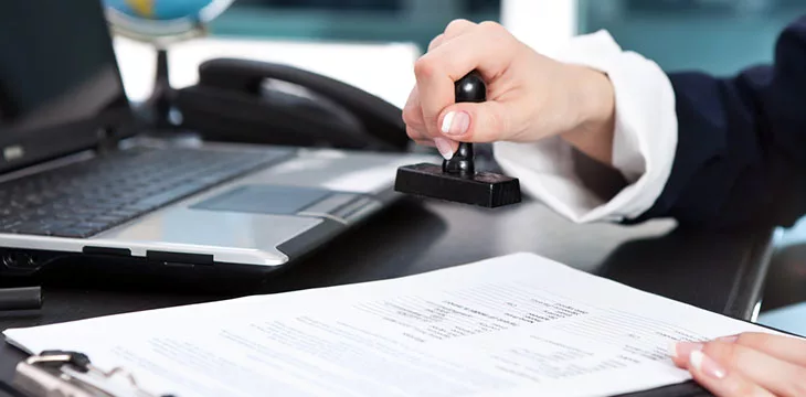 stamping document on desk beside a laptop