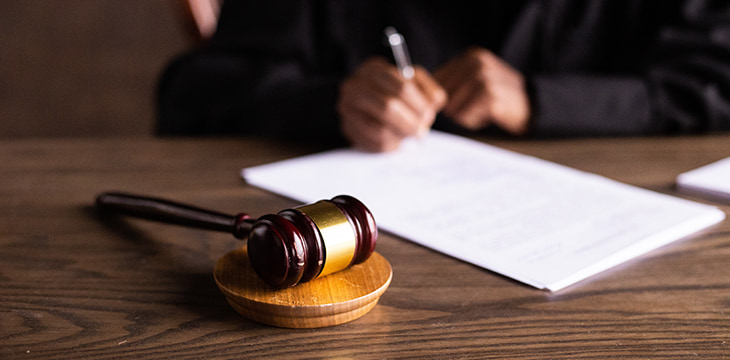 A gavel on a table with a man writing on white paper in the background