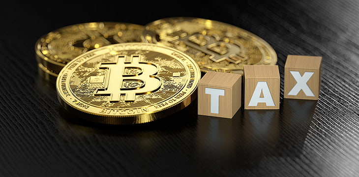 Stack of Bitcoin laying next to wooden blocks with TAX letters. Bitcoin investments and taxes concept.