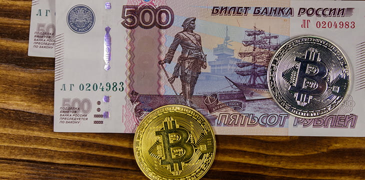 Golden and silver bitcoins and five hundred russian rubles bills on wooden background