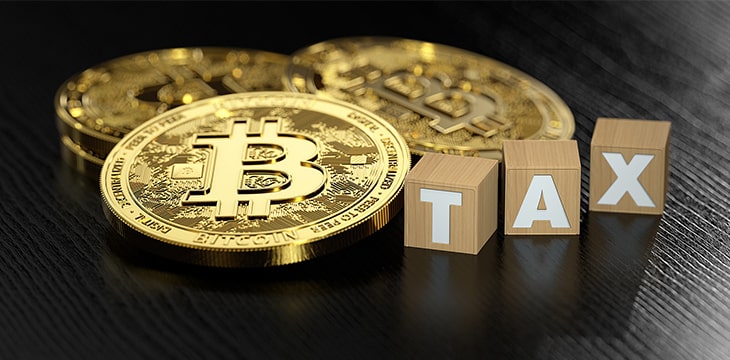 Stack of Bitcoin laying next to wooden blocks with TAX letters.