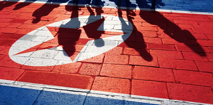 Shadows of group of people walking through the ground with North Korean flag