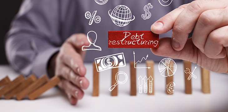 Hand holding red domino with debt restructuring word written in chalk.