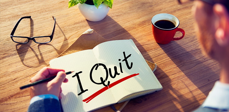 Man writing I Quit on notebook on desk