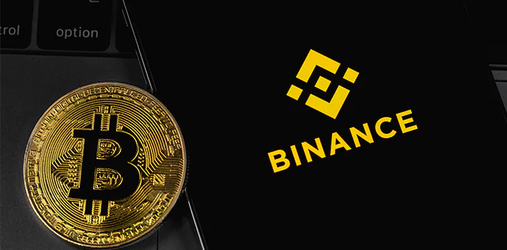 Bitcoin next to smartphone with Binance logo on top of laptop