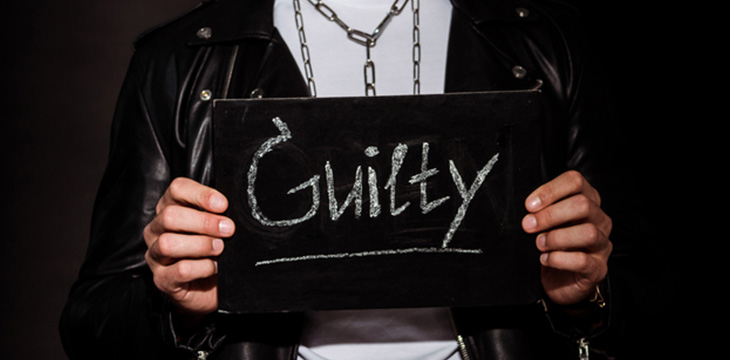 man holding chalk board with guilty word written