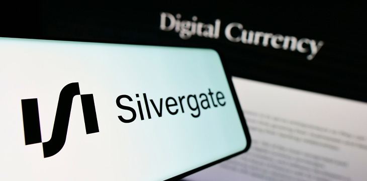 Hand holding the smartphone in front of the PC screen with the symbol of Silvergate