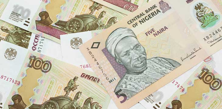 A close up image of a peach colored, five Nigerian naira bank note on a background of Russian one hundred ruble bank notes