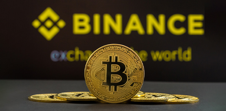 A big Bitcoin cryptocurrency coin in the center and other bitcoin coins from both side in front of Binance crypto market