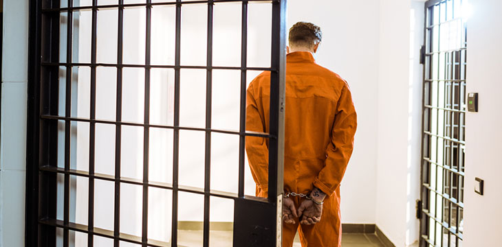 Back view of prisoner standing in handcuffs outside prison cell corridor