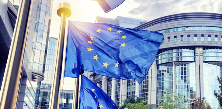 EU flags waving in front of European Parliament with sun rays shining through