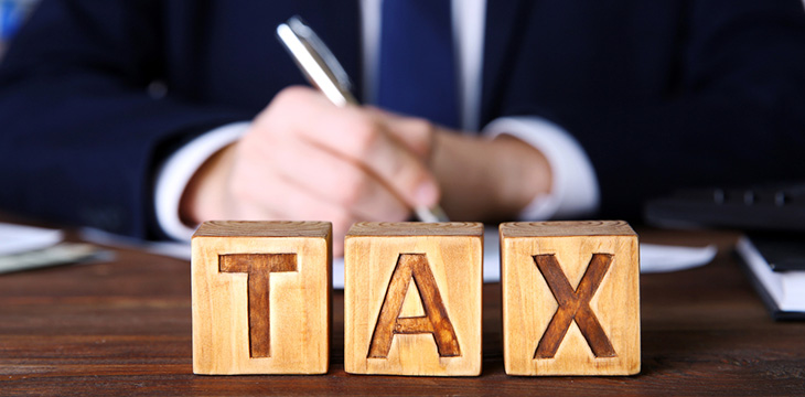 Wooden cubes with word TAX with man in a suit behind it