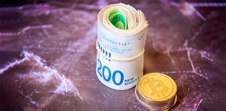 Roll Israeli Shekel ILS banknotes near cryptocurrency tokens Bitcoins