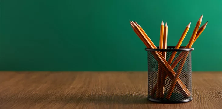 Pencils on wooden table with green chalkboard on background