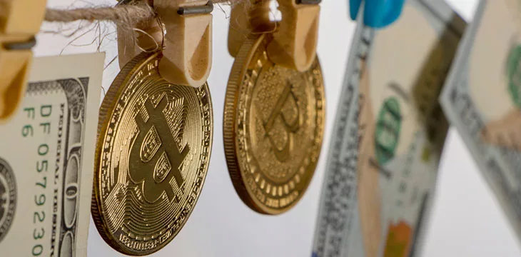 yellow clothes peg holding gold bitcoins and dollar bills