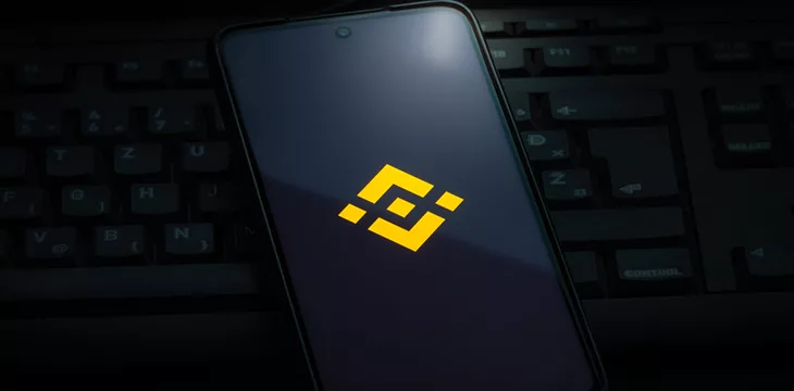 Binance exchange logo on smartphone screen laying on computer keyboard