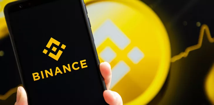 Binance mobile app running at smartphone screen with Binance logo at background.