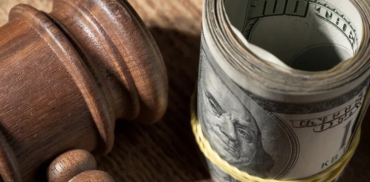 US dollar bills rolled together next to judge's gavel.