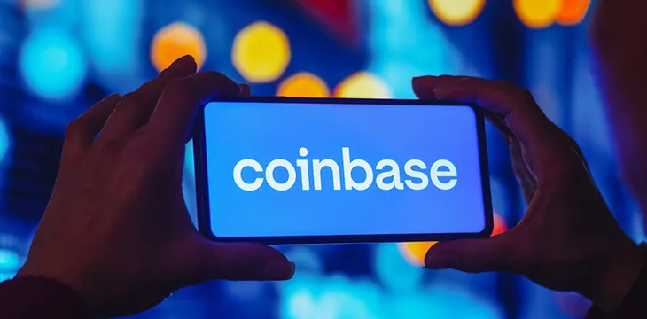 two hands holding a smartphone with coinbase logo on screen