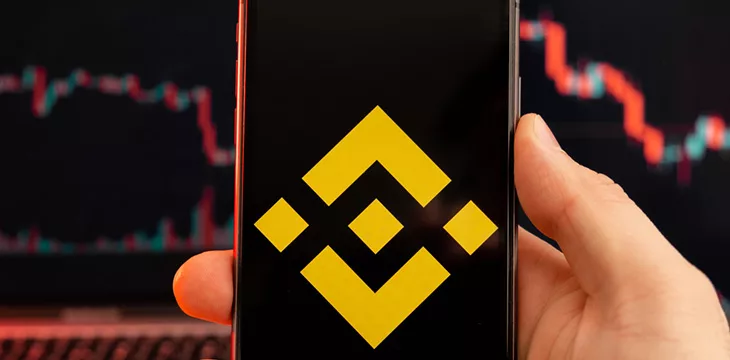 BNB app of cryptocurrency stock market analysis on the screen of mobile phone in man hands and downtrend charts trading data on the background