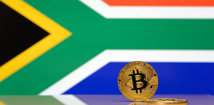 Golden bitcoin stands on a blurred background of state flag of South Africa