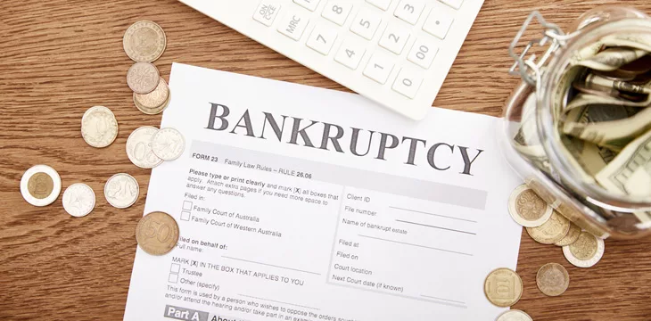 Top view of bankruptcy form, coins, calculator and glass jar with dollar banknotes on wooden table