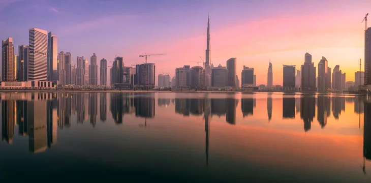 Cityscape of Dubai and panoramic view of Business bay with reflection of skyscrapers on water during purple sunrise, UAE