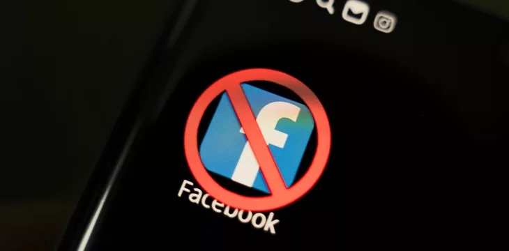 A crossed-out icon on a black smartphone screen-concept of banning the application facebook