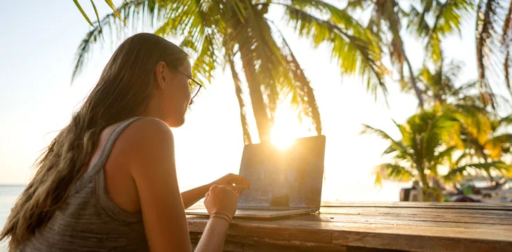 Girl freelancer working on the sea at sunset with a computer digital freelancer nomad concept