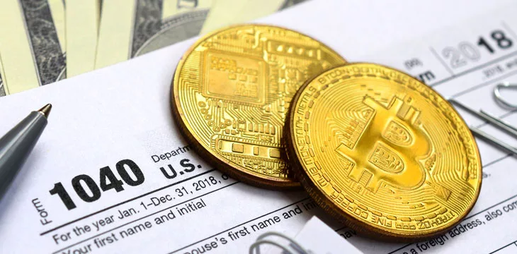 Pen, bitcoins and dollar bills is lies on the tax form 1040 U.S. Individual Income Tax Return