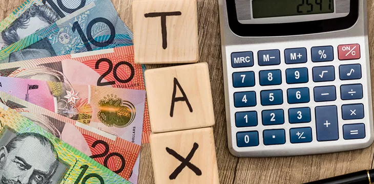 Tax word on wooden cubes with Australian bank notes, pen, and calculator