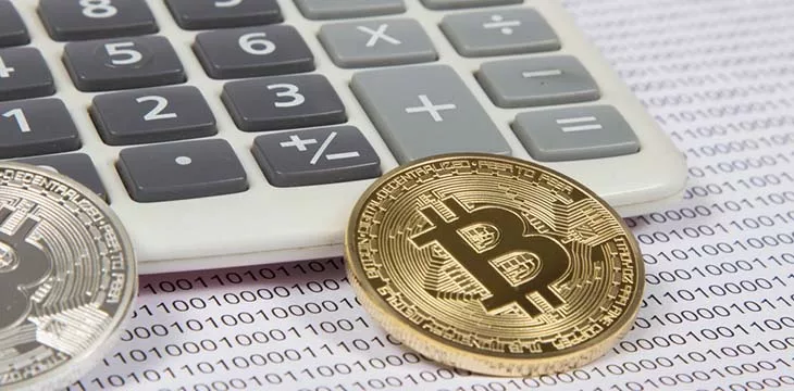 gold and silver bitcoin in front of a calculator