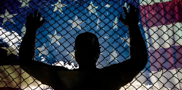 Silhouette standing near wire with american flag